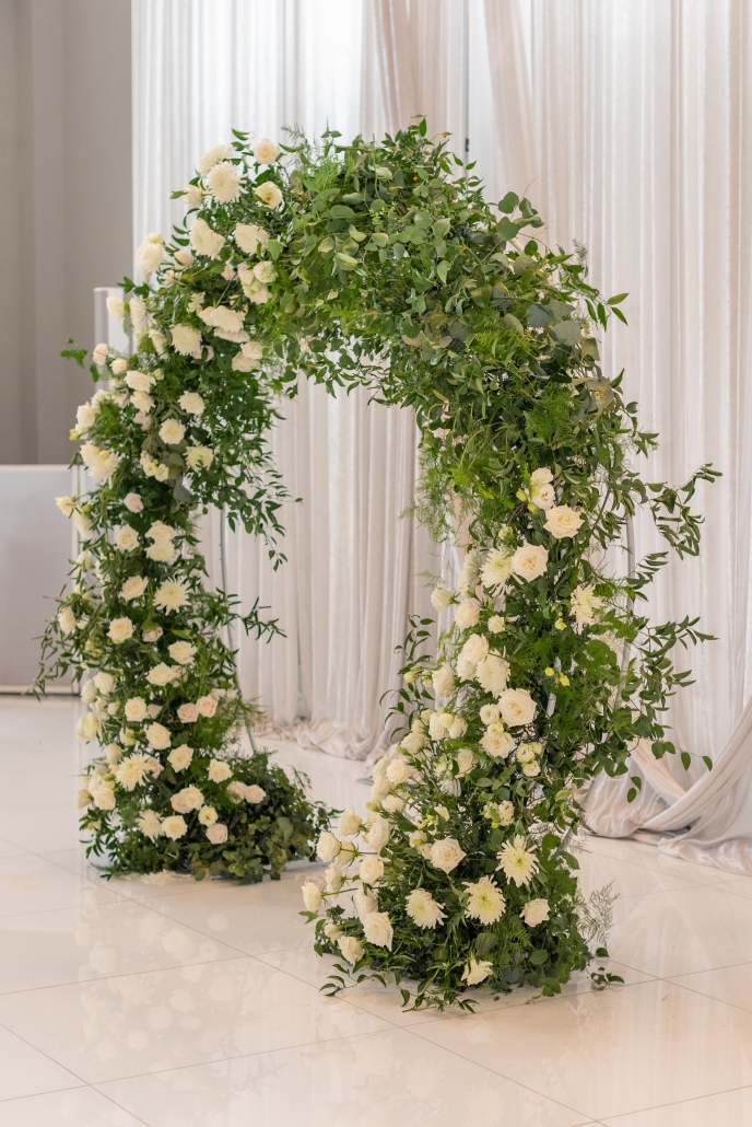 Rounded floral ceremony arch with greenery and white blooms.