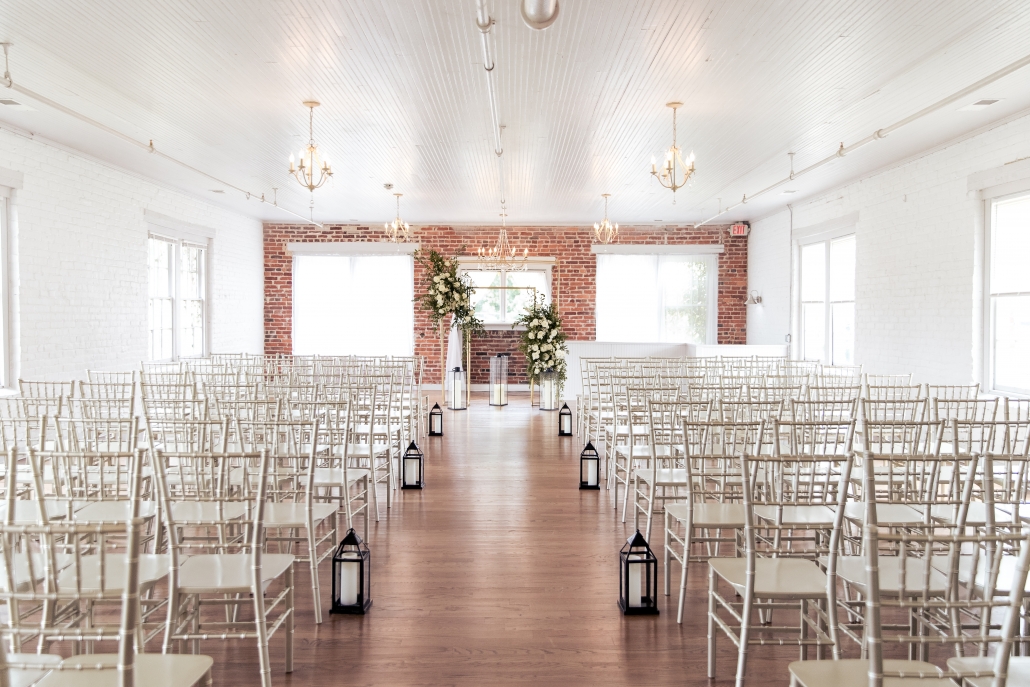 Elegant mill indoor wedding reception with white chairs and floral backdrop